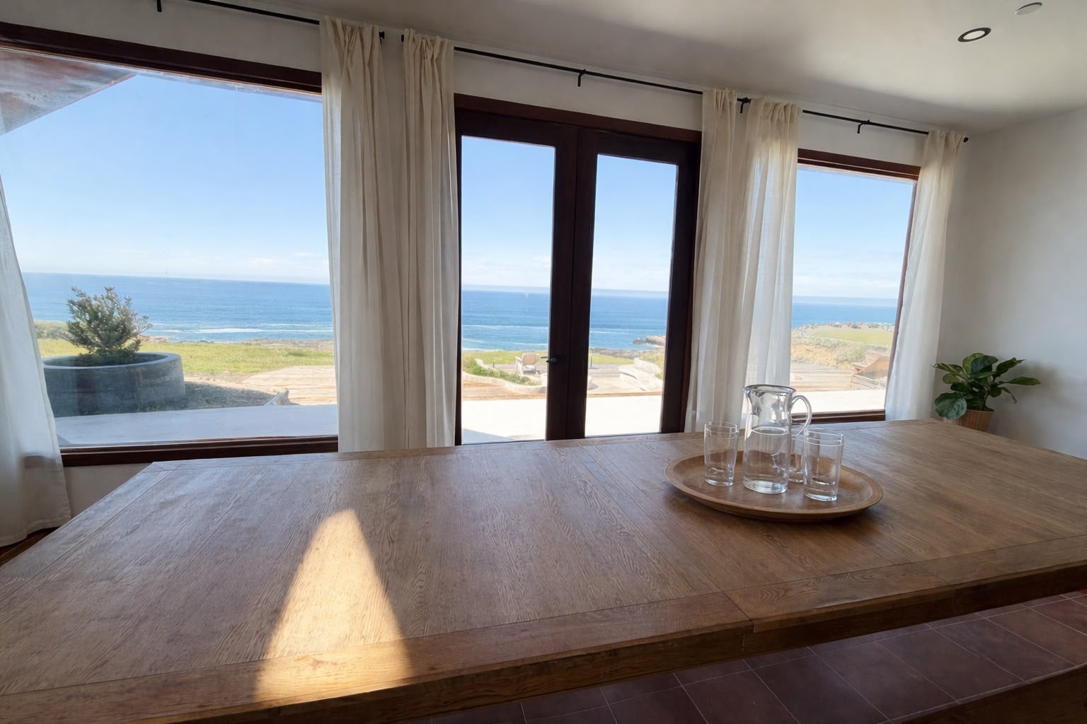 A dining table framed by wide windows overlooking the ocean